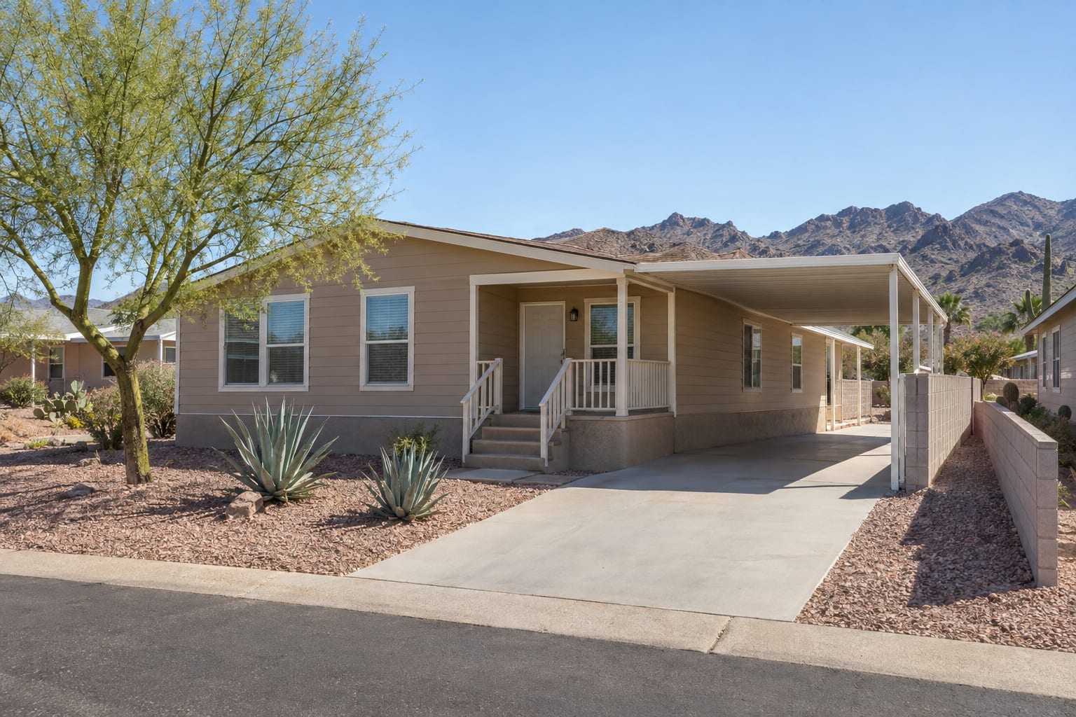 A double-wide manufactured home with a carport on its own lot in an Arizona subdivision, with a low block wall along the lot line.
