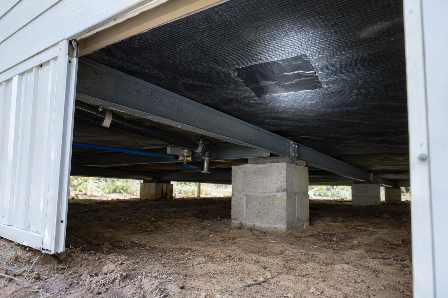 The black belly wrap under a manufactured home, lit by a flashlight through an open skirting panel, with a taped patch over a repair.