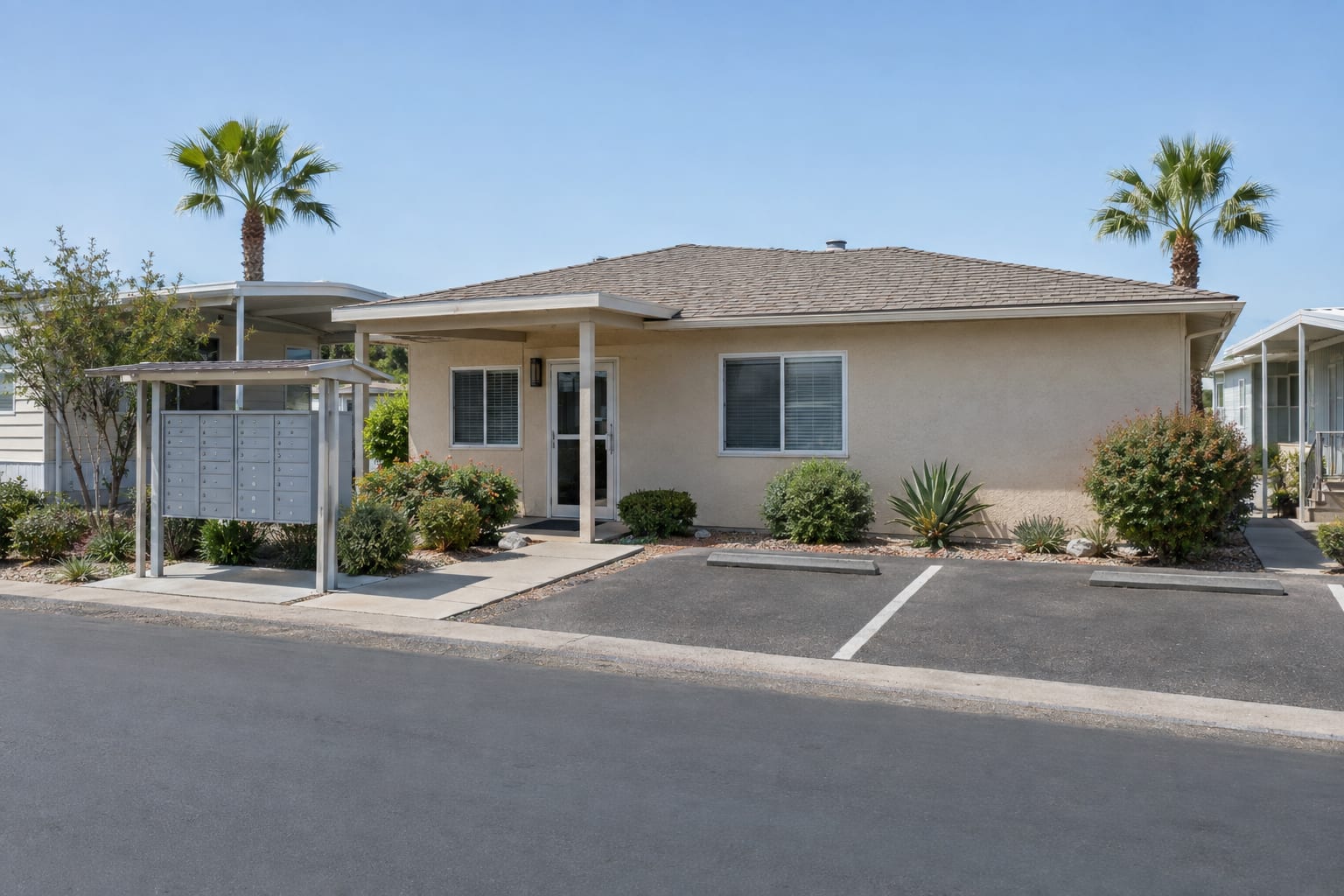 A small single-storey community office with a covered entry and a bank of cluster mailboxes, with manufactured homes behind it.