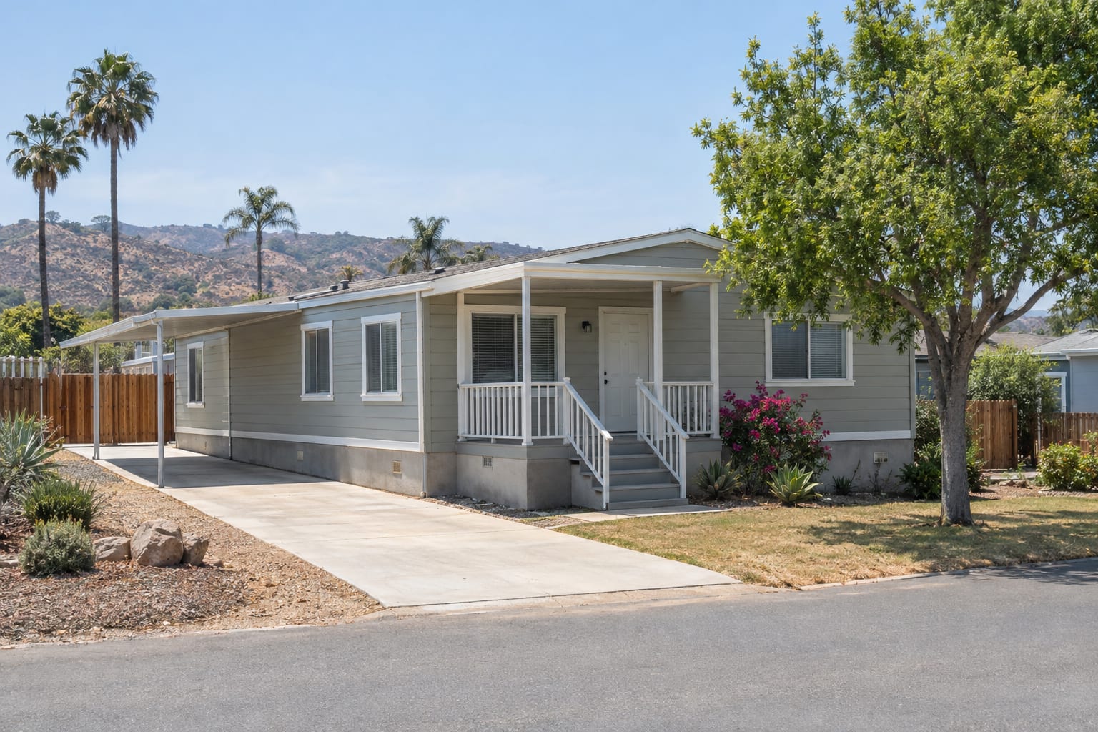 A manufactured home on a low concrete perimeter foundation on a fenced lot beside a quiet county road in inland California