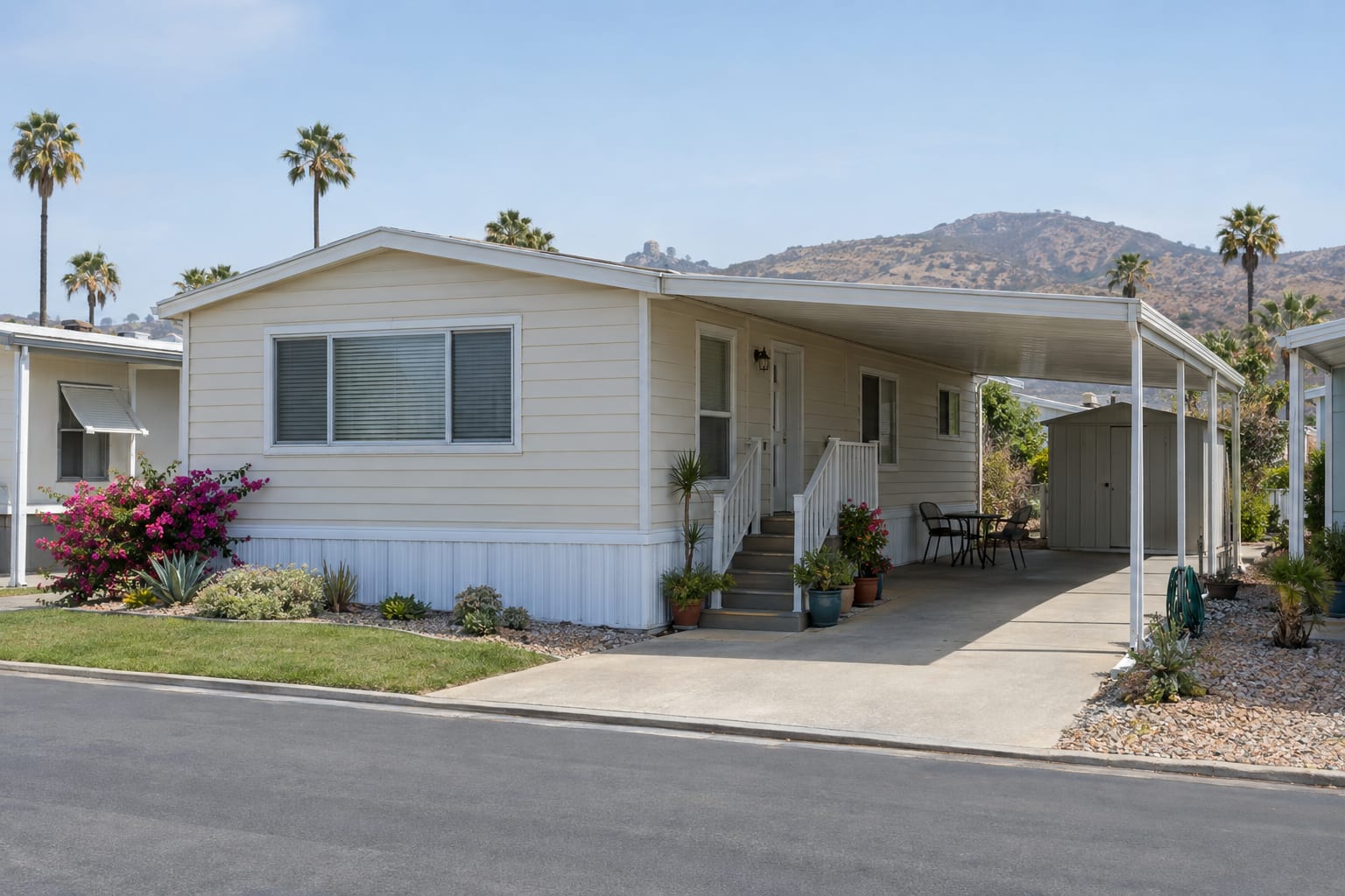 A lived-in manufactured home on its space in a community, with a patio set under the carport and a small storage shed