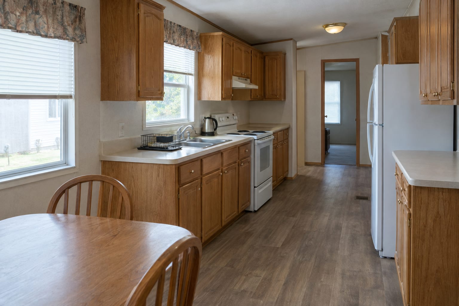 An older manufactured home kitchen with original oak cabinets and laminate counters, clean and in working order.
