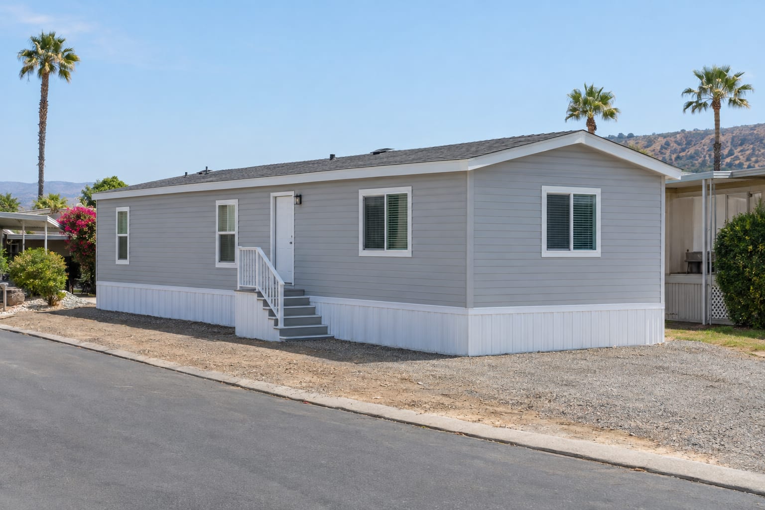 A newly installed manufactured home with fresh skirting and entry steps on a bare graded space, between established homes.
