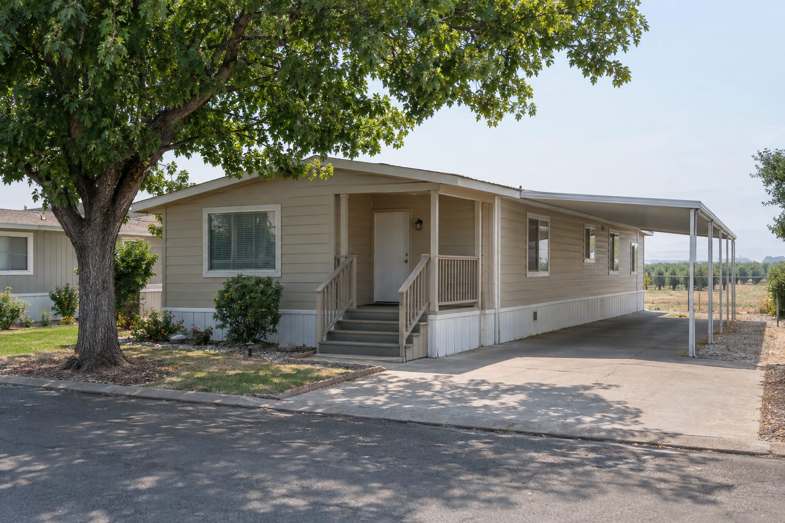 An older double-wide manufactured home on a tree-shaded space in an established Central California community, late-morning light