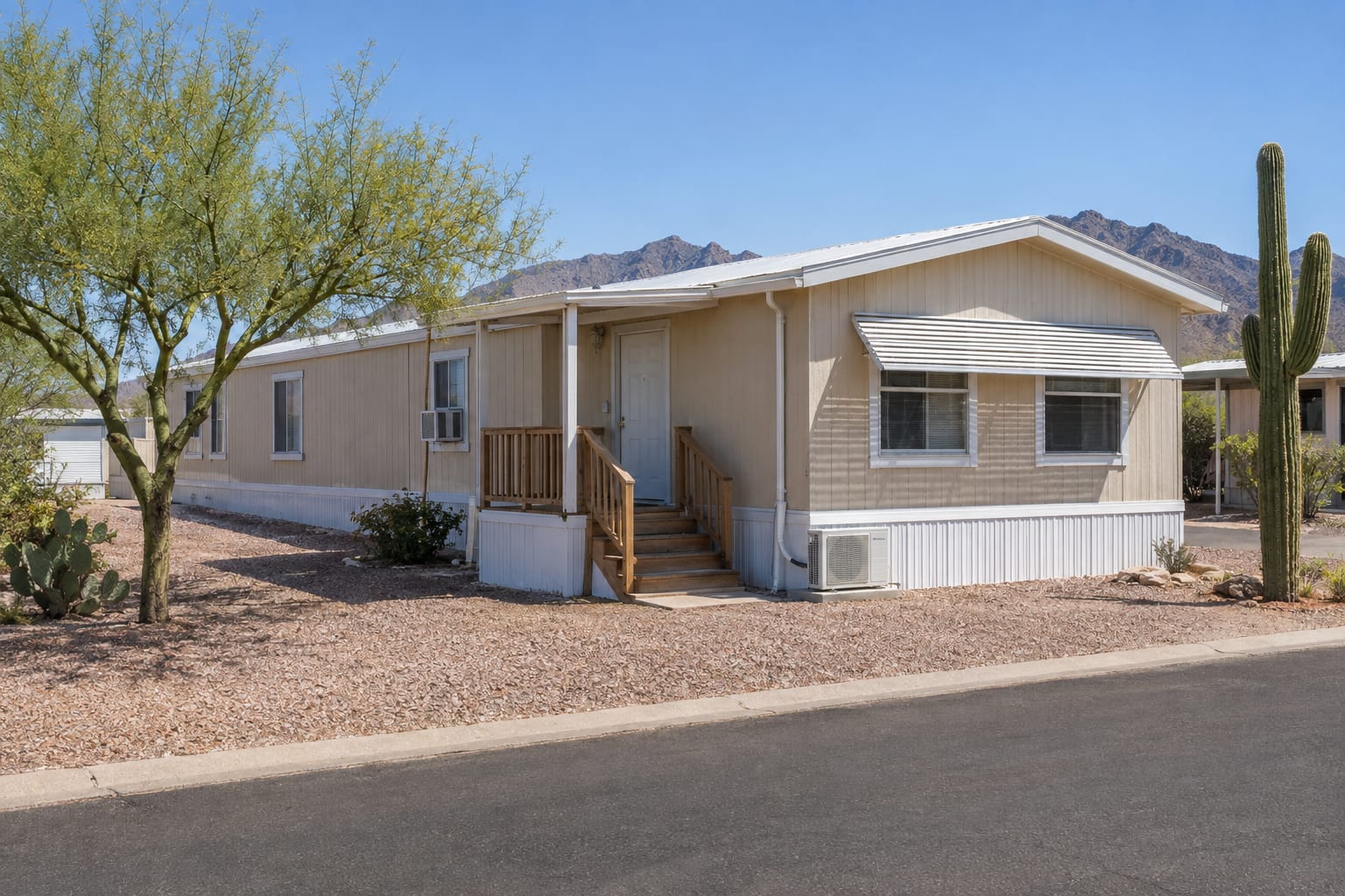A single-wide manufactured home in a Phoenix-area community with a mini-split condenser on a pad beside it, a window air conditioner, and a shade awning over the west-facing windows
