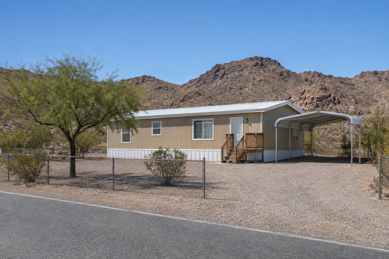 A single-wide manufactured home with a metal carport on its own gravel lot in rural Arizona, with rocky hills behind.